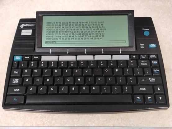 Chunky black device with MailStation label.  It houses a screen and horizontal qwerty keyboard and is about the size of a hardback textbook.  It is displaying a screenful of dumped hex.  The command 4100,417e is visible at bottom of screen.