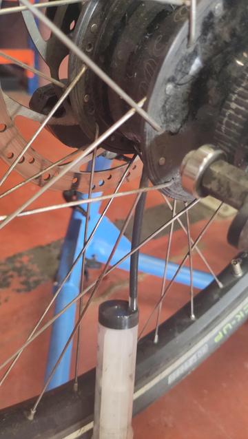 Gros plan sur un moyeu de vélo avec une seringue qui y est raccorde et un liquide noir qui coule dedans