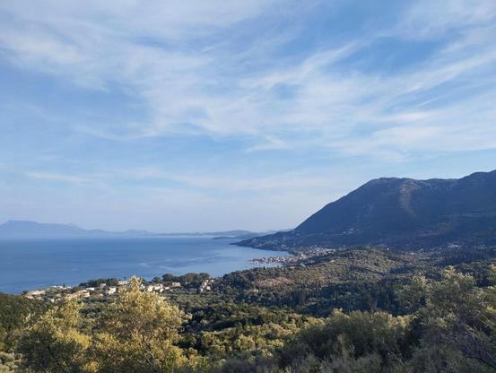 A landscape photo with a view into the distance over the Ionian Sea and the landscape along the wooded mountainous coastline of the island of Lefkada on a summer's day.

Ein Landschaftsfoto mit dem Blick in die Weite über das Ionische Meer und die Landschaft entlang der bewaldeten bergigen Küstenlinie der Insel Lefkada an einem Sommertag.