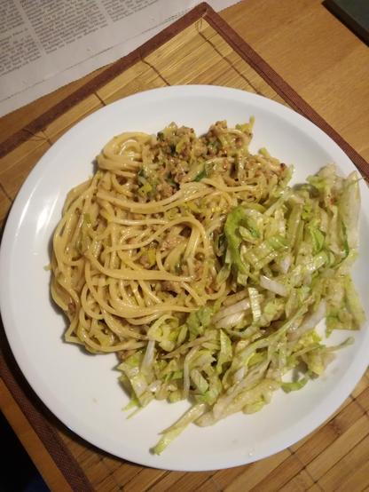 Auf einem braunen Platzset steht ein weißer Teller.
Darauf links die beschriebene Pasta und rechts der Salat.