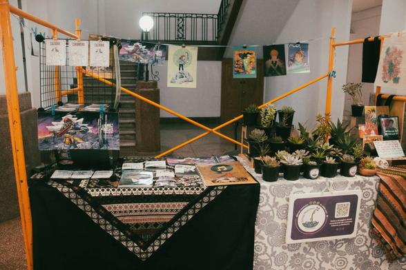 Fotografía, plano general de un stand en "Otro Bazar", parte de las actividades de Sábado en LabNL. El espacio se encuentra compartido entre Fixionauta (taller de ficciones gráficas) y Linaje Mexicano (venta de suculentas).