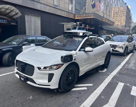 Autonomous Waymo white four door, with driver, front view, midtown Manhattan.