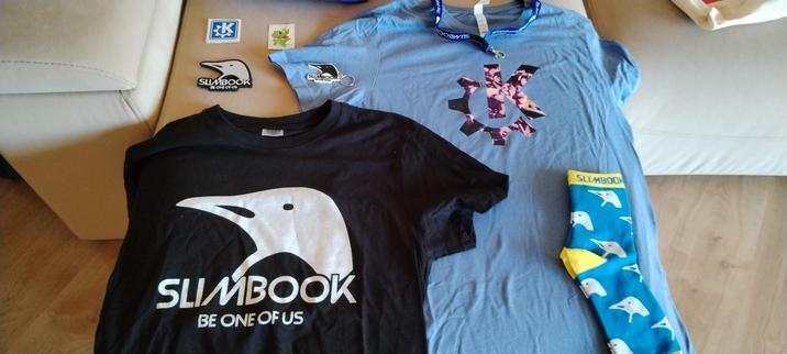 Foto de los regalos que menciono en el toot
La camiseta de Slimbook es negra con su logo y nombre
La camiseta de AkademyES tiene una K coloreada.
