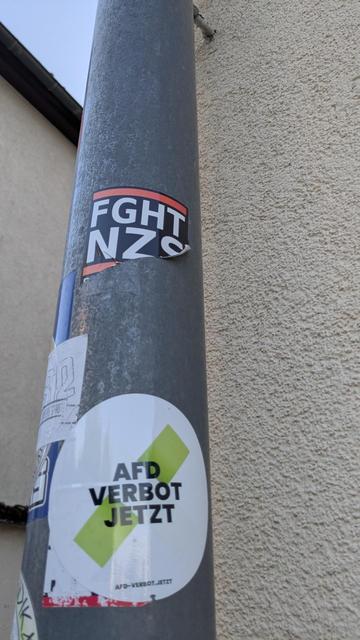 Fallrohr einer Regenrinne, mit ein paar Stickern beklebt, sehr hoch hängt ein FGHT/NZS Sticker der versucht wurde abzureißen, aber immer noch gut sichtbar und lesbar ist.