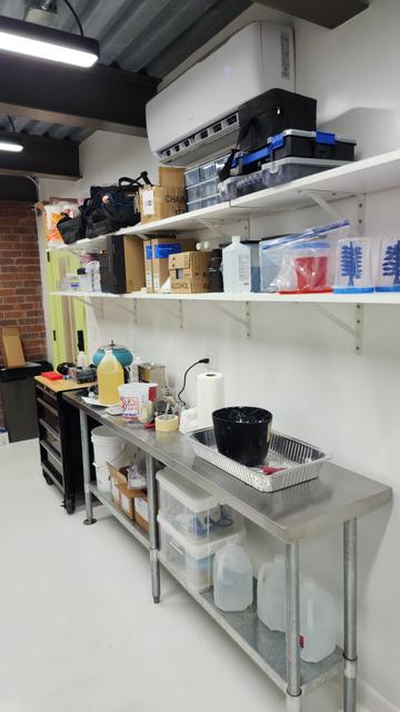 Back wall of a jewelry studio featuring shelving and work bench full of tools and equipment. The studio is brightly lit and painted white to aid with the detailed precision work of creating our intricate designs.