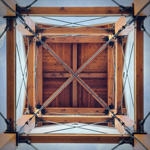 A small, wooden tower is viewed from directly underneath against a blue morning sky.
