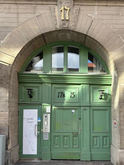 An arched doorway in a stone building, with a 3-panel green wooden door. The street number above the arch reads 17.