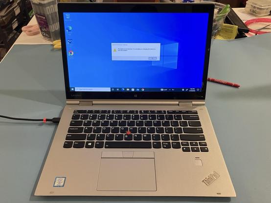 A silver Lenovo Thinkpad Yoga X1 has an error message on the screen which says, "The battery is not detected. Try reinstalling or recharging the battery to solve the problem.