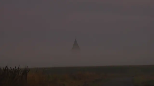 Aus einer Nebelbank schaut die Spitze eines alten Wasserturms heraus