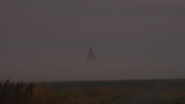 Aus einer Nebelbank schaut die Spitze eines alten Wasserturms heraus