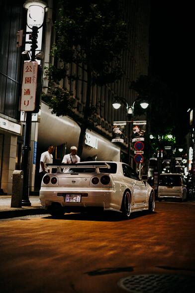photo of a white Nissan Skyline parking at the side of a nightly street