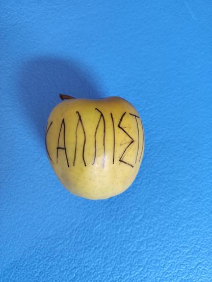 A golden apple with letters in ancient greek: Kallisti - To the Most Beautiful. On a blue ground.