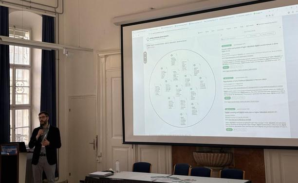 Peter Kraker giving a presentation at the Open Science Festival 2025. Behind him is a large screen showing a knowledge map that is zoomed into an area related to digital transformation.