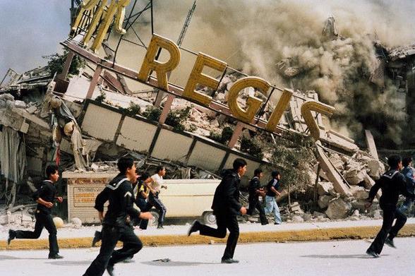 Hombres corriendo en una calle mientras un edificio colapsa durante el terremoto de 1985 en Ciudad de México, con humo y escombros en el aire.
