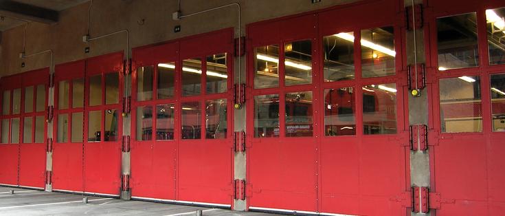 Five red doors with windows in the upper halves line the fire station garage. Through the windows you can see fire trucks. Seattle, Washington.