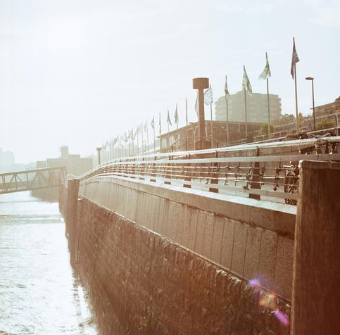Kai an den Landungsbrücken, hartes Gegenlicht, aber das Geländer macht einen hübschen Bogen und die Fahnen vom Biergarten wehen im Wind