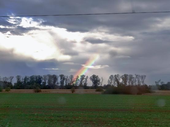Foto von einem Regenbogen der durch dicke Wolken sticht.