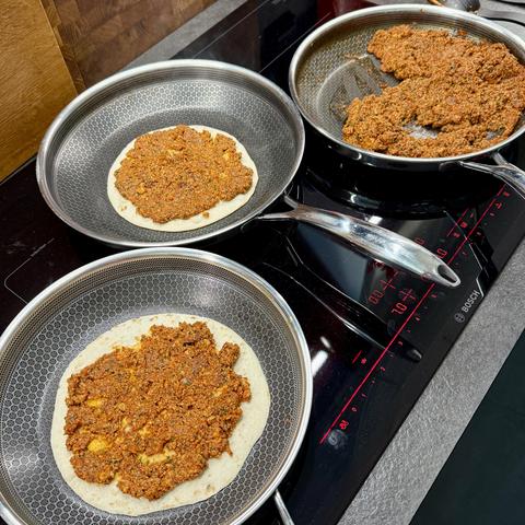 Lahmacun preparation at the cooker with three pans on the go, one for the sauce and two with wraps and sauce on top.