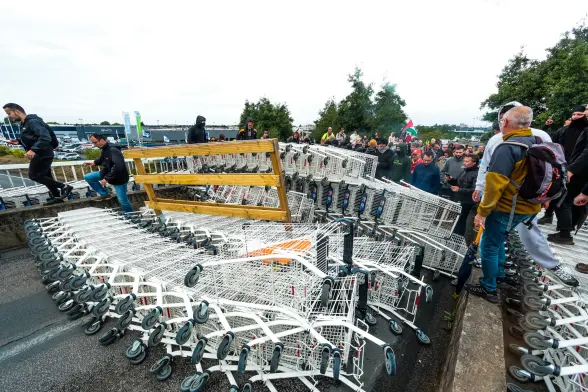 Sur un pont au-dessus du périphérique de Niort, une barricade constituée de rangés de chariots de supermarché, certaines rangées sont empilées les unes sur les autres.
Des manifestants sont derrières et sur le côté de la barricade.
On peut voir une personne tenant un drapeau palestinien parmi les manifestants.