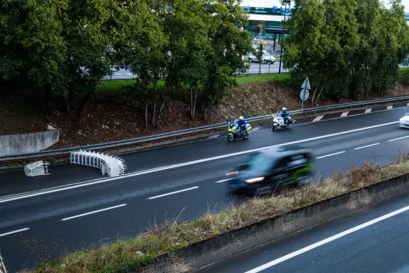 Une rangée de chariot de supermarché sur une voie de sortie du périphérique de Niort, menant à la zone commerciale Mendès-France.
Deux motards de la police sont stationnés 10 mètres avant.
Des voitures roulent sur le périphérique.
On peut apercevoir derrière les arbres situés sur le côté de la voie du périphérique, l'enseigne Leclerc.