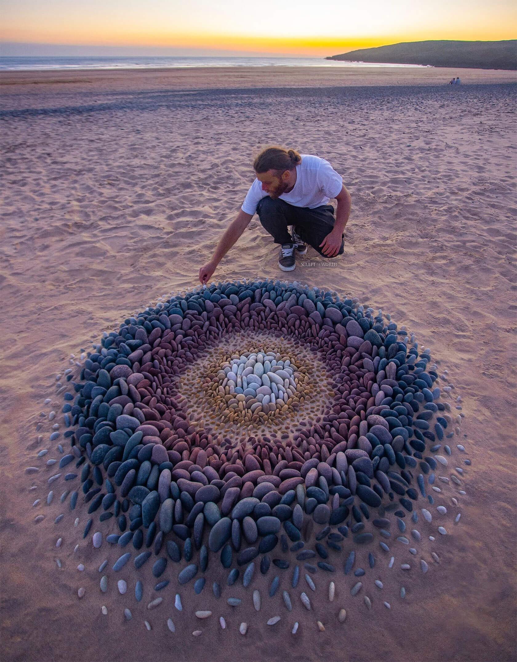 A person arranging colorful stones in a circular pattern on a sandy beach at sunset, creating a stunning natural artwork.