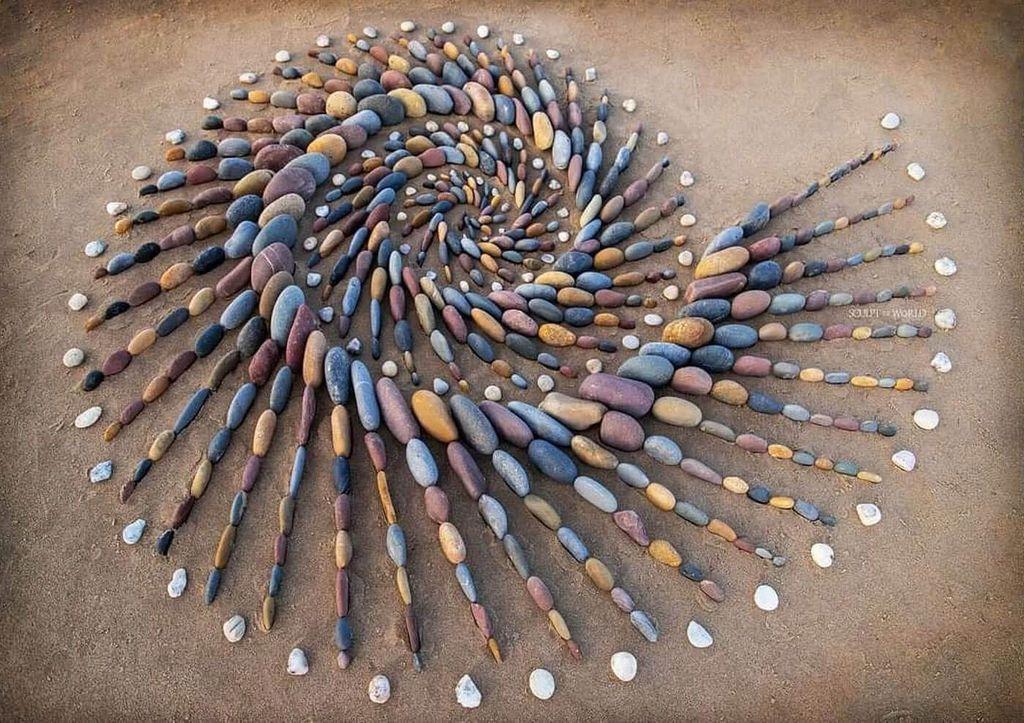 Spiral arrangement of colorful stones radiating outwards, creating a mesmerizing, natural art piece on a sandy surface.