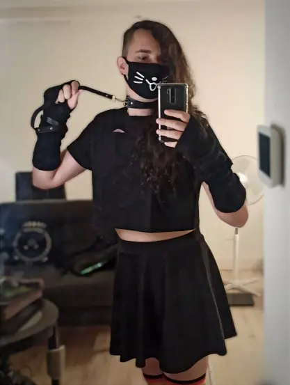 Selfie in a mirror of a person with long black hair, in a cat facemask, wearing miniskirt, crop top and collar