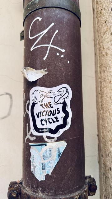 Sticker on a water pipe representing a cartoonish hand linked to foot by a black limb and is ticking the foot with a feather. The text on the sticker says «  The Vicious Cycle » by NoeGrit