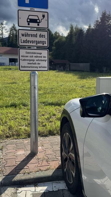 Parkplatz zum Laden von Elektroautos. Zusatzschild: „Elektrofahrzeuge müssen sich während des Ladevorgangs vollständig innerhalb der Bodenmarkierung befinden“