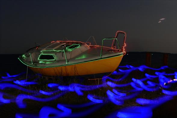 In einer hellen Nacht lagert auf einer am Bodden gelegenen Wiese schief ein altes Segelboot ohne Mast. Die während der Langzeitbelichtung gemalten Lichtzeichnungen lassen es so wirken, als fahre das Boot durch die unruhige See. Verwendet wurde hierfür ein einfarbiges Smartphone-Display. Seine Konturen sind mit grünen und roten Strichen nachempfunden, und seinen Rumpf leuchtet eine Lampe an. So ergibt sich eine friedliche, doch gleichzeitig abstrakt-komische Szenerie.