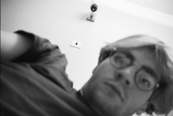 A blurred selfie of someone a long time ago, bleached hair, with what looks like a light or a camera behind an in focus.