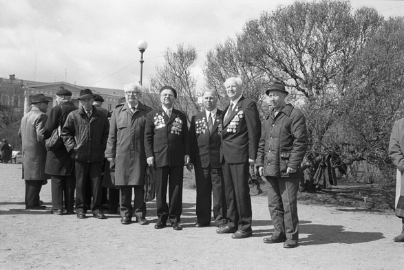 Some old men posing with lots of medals on their chests.  A black and white photo.  A big leafless tree behind.