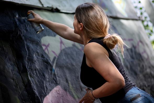A spraycan artist holding a can and painting a wall. 
The angle of the shot and the position of the artist is really dynamic.