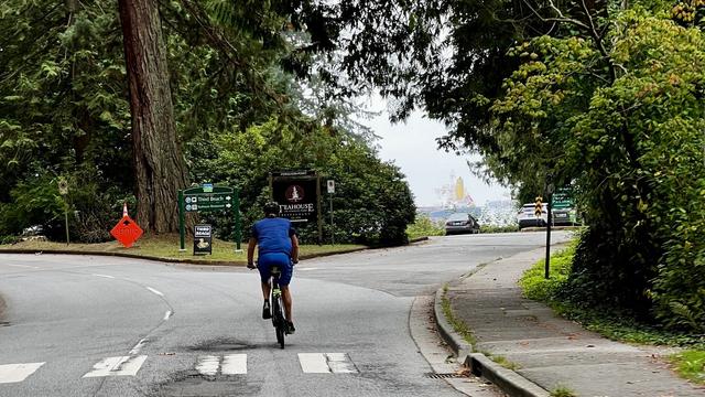 A single cyclist on a two-lane blacktop where it splits to enter a parking lot.