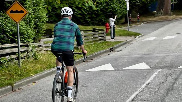 A single cyclist on a two-lane blacktop where it crosses a pedestrian path.