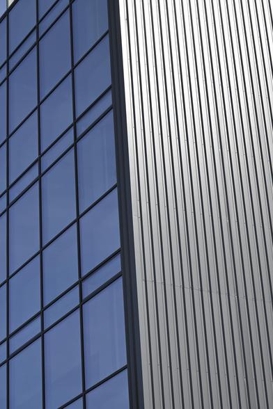 Modernes Gebäude, Links eine Fensterfront und Rechts die Gebäudehülle bestehend aus Dunkelgraue Bleche