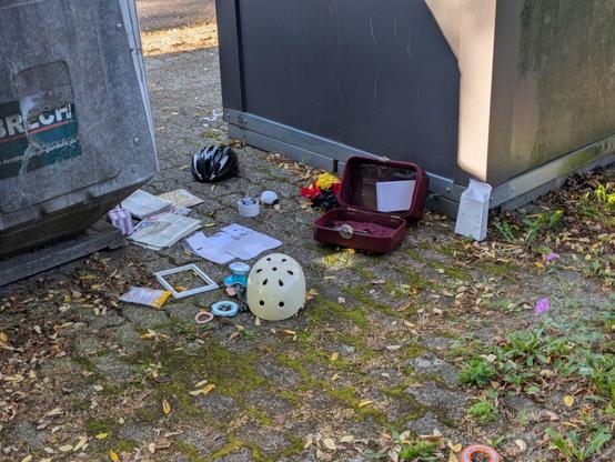 Foto von Müll auf dem Boden neben dem Glas- und Altkleider Container. Dabei handelt es sich um Plastikmüll und Altpapier.