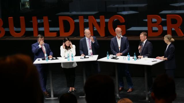 Auf dem Foto ist eine Podiumsdiskussion mit sechs Teilnehmenden auf der Konferenz Building Bridges 2025 in Dresden Hellerau zu sehen. Die Diskussion trägt den Titel „Connecting Science und Politics“. Am zweiten Tisch von rechts spricht Michael Kretschmer, Ministerpräsident des Freistaates Sachsen, ins Mikrofon. Zweite von links ist Reghina Valutyte, Vize-Ministerin für Bildung und Wissenschaft der Republik Litauen, die aufmerksam zuhört. Die Bühne ist mit großen roten Buchstaben „BUILDING BRIDGES“ dekoriert, auf den Tischen stehen Wasserflaschen und Mikrofone.
Hinweis: Foto: Cyberagentur