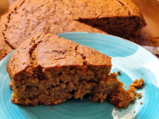 Der Kuchen, frisch aus dem Ofen, angeschnitten, ein Stück auf türkiesen Teller, der ganze restliche Kuchen im Hintergrund