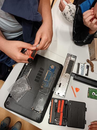 Ordinateur portable ouvert par en dessous avec deux élèves au-dessus dont l'un tient un tournevis.