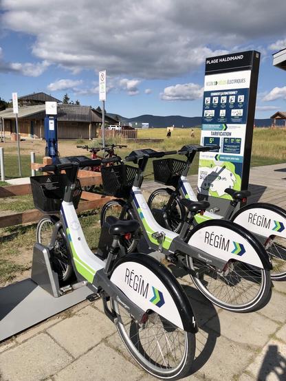 Une station de vélo-partage près de la plage d'Haldimand, à Gaspé. On y voit trois vélos électriques avec des paniers