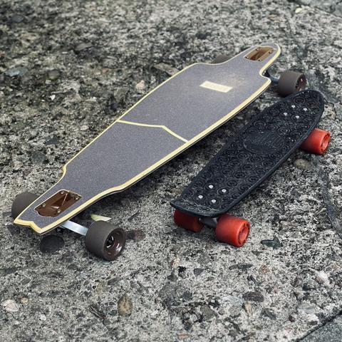 Links ein Globe Prowler Longboard, rechts daneben ein kleines Pennyboard - Goldcup Banana Board stehen auf altem und groben grauen Betonboden