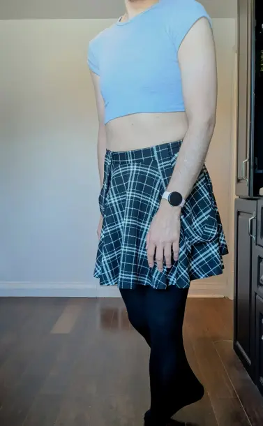 A stand slightly turned with black stockings and the same black plaid skirt. My arms are at my sides. I'm wearing a fitted light grey cropped tshirt