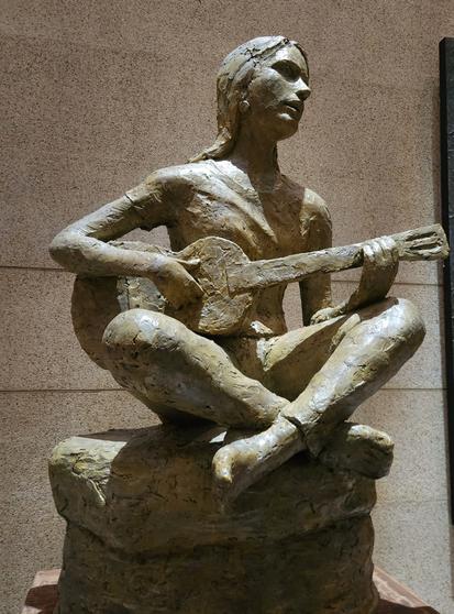 A painted plaster sculpture of Joan Baez sits cross-legged, playing the guitar.
