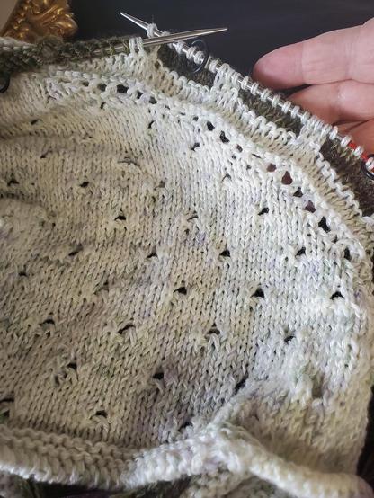 My progress on shawl so far, soft white and deep green, circular needles crossed, a bit of my hand to the right