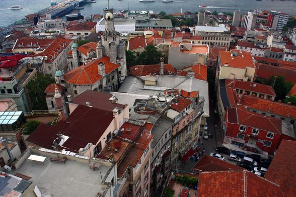 Looking down on the red tile roofs of houses and businesses in Istanbul, Turkey. The buildings are close together, and the street configuration is complicated (no real grid). Bosphorus river is just visible at the top of the image.