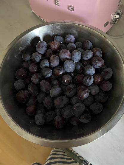 Tummia luumuja metallikulhossa