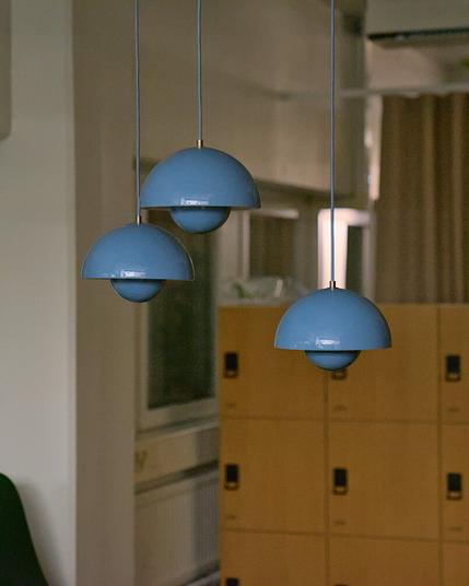 A photograph of three suspend blue metallic lamp shades, at different heights. Their shapes are two half spheres, one big on the top, one small on the bottom. In the background storage lockers and windows letting no light through, because it is night time.