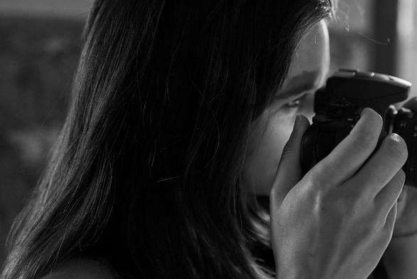 Eine junge Frau blickt in den Sucher ihrer Kamera. Ihr Gesicht wird dabei vom Display der Kamera beleuchtet.