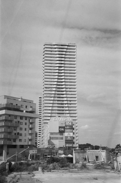 Hier sieht man das Citygate am Ende der Wagramer Straße, Donaustadt, Wien. Die Schlieren auf dem Fenster der U1 gehen nahtlos auf die Fassade des Hochhauses über. Der Berg am Horizont ist übrigens ein Müllberg. Ohne Müllberge wäre es hier eben wie im Rest des Marchfeldes.